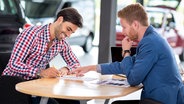 Verkäufer mit Kunden bei der Vertragsübergabe im Autohaus. © Fotolia.com Foto: luckybusiness
