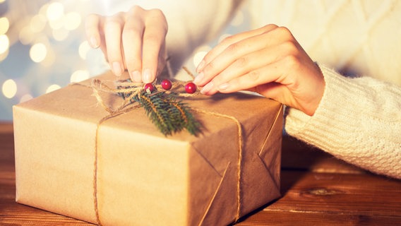 Eine Frau packt und verziert ein weihnachtliches Päckchen. © imago images / agefotostock Foto: dolgachov
