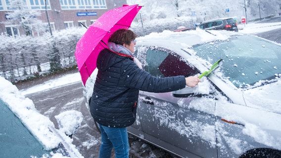 Eine Frau mit Regenschirm befreit ihr Auto von Schnee, © dpa-Bildfunk Foto: Daniel Bockwoldt
