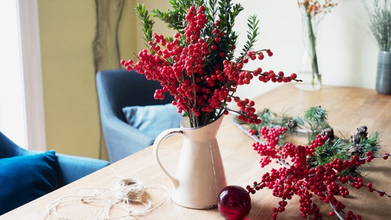 Eine Vase mit roten Ilex-Beeren und grünen Myrte-Zweigen steht auf einem Tisch.  Foto: Anja Deuble