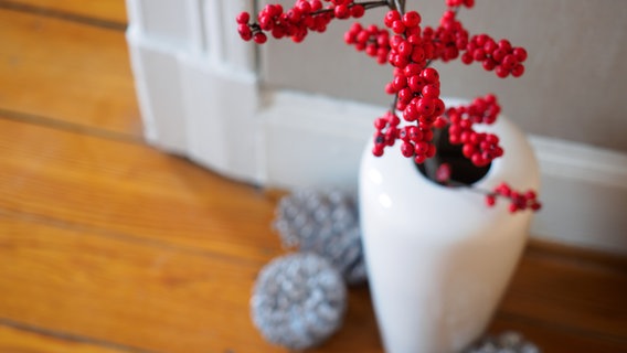 Ein Zweig mit roten Beeren steht in einer weißen Vase auf einem Holzfußboden.  Foto: Anja Deuble