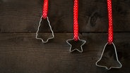 Drei Plätzchen-Ausstecher hängen an rot-weißen Geschenkanhängern vor einer dunklen Holzfläche. © Photocase Foto: Macroart