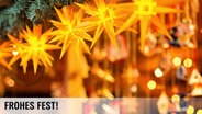 Beleuchtete Sterne hängen an einer Weihnachtsmarkt-Bude, im Hintergrund sind Weihnachtsdeko-Artikel zu erkennen. © Fotolia Foto: Fotimmz