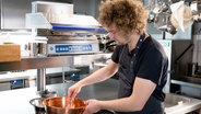 Koch Marianus von Hörsten steht in seiner Restaurantküche und rührt in einem Kupferkessel. © NDR Foto: Claudia Timmann