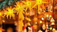 Leuchtende gelbe Sterne und verschiedene Anhänger an einer Bude auf einem Weihnachtsmarkt. © Fotolia Foto: Tim Mueller-Zitzke