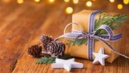Ein Weihnachtsgeschenk und Sterne auf einer Holzplatte, Lichterglanz im Hintergrund. © Fotolia Foto: Floydine