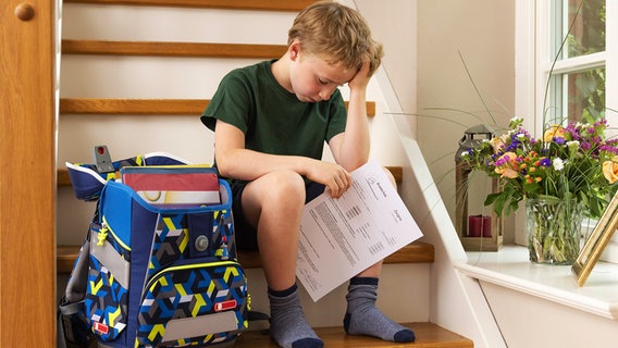 Ein enttäuschter kleine Junge sitzt mit seinem Zeugnis auf der Treppe. © Imago Foto: Bernhard Classen