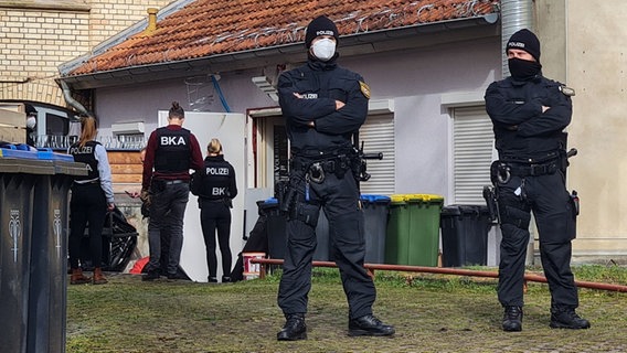 Polizisten stehen vor dem Hintereingang eines Gebäudes, das sie durchsuchen. © picture alliance/dpa/Martin Wichmann TV 