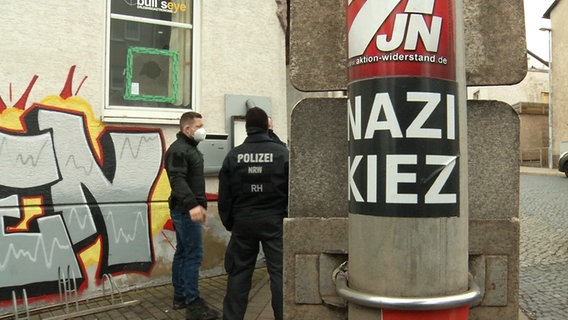 Polizisten stehen vor einem Gebäude. An einem Pfahl ist ein Aufkleber mit der Aufschrift Nazi Kiez zu sehen. © Martin Wichmann TV/dpa 