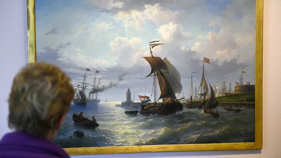 Eine Person schaut auf ein Gemälde mit Schiffen und goldenem Rahmen. © picture-alliance/dpa 