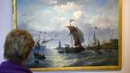 Eine Person schaut auf ein Gemälde mit Schiffen und goldenem Rahmen. © picture-alliance/dpa 