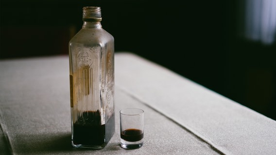 Eine Flasche Schnaps steht auf einem Holztisch, daneben ein benutztes Trinkglas. © Photocase Foto: Eliza
