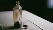 Eine Flasche Schnaps steht auf einem Holztisch, daneben ein benutztes Trinkglas. © Photocase Foto: Eliza