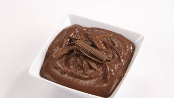 Ein Schokoladenpudding in einer Glasschale mit einem Löffel und echten Schokoladenstückchen. © Imago 