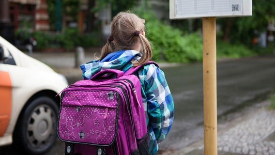 Ein Mädchen mit Schulranzen steht an einer Haltestelle und wartet auf einen Bus. (Symbolbild) © picture alliance Foto: Silvia Marks