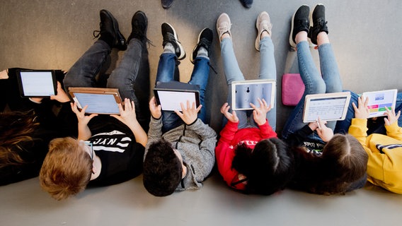 Schülerinnen und Schüler einer 7. Klasse sitzen an eine Wand gelehnt und lernen mit iPads. © picture alliance/dpa/Julian Stratenschulte 