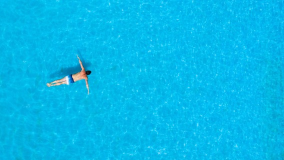 Ein Mann schwimmt im blauen Wasser. © picture alliance/dpa | Julian Stratenschulte 