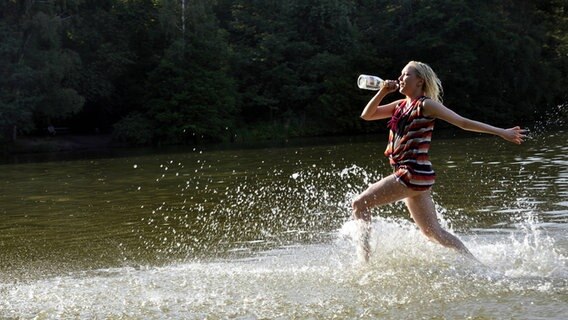 Eine Frau läuft durch einen See und trinkt aus einer Sektflasche © Imago 