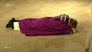 Bischof Bode liegt in der Kirche mit dem Bauch auf dem Boden. © screenshot 