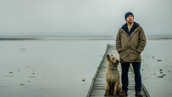 Sörensen (Bjarne Mädel) steht auf einem Holzsteg. Neben ihm sitzt ein Hund. © NDR/Michael Ihle Foto: NDR/Michael Ihle