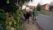 Ein Bauer läuft mit einer Kuh durch ein Dorf.  