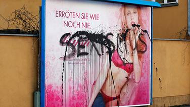 Das Wort "Sexismus"  steht mit schwarzer Farbe geschmiert auf einer Plakatwerbung für Unterwäsche. © dpa bildfunk Foto: Wolfram Steinberg