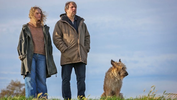 Sörensen (Bjarne Mädel) schaut mit einer Frau in die Ferne, der Wind zaust in den Haaren, daneben sitzt ein pelziger Hund - Szene aus "Sörensen fängt Feuer" © NDR/ Michael Ihle Foto: Michael Ihle