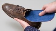 Ein Mann legt eine Einlegesohle in einen Halbschuh (Symbolbild). © picture alliance Foto: Andrea Warnecke