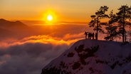 Eine Gruppe von Menschen steht auf einer Bergkuppe vor einem goldenen Sonnenuntergang. © Photocase Foto: AntonRussia