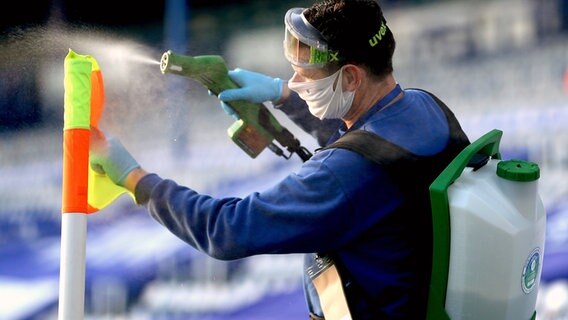Ein Mann mit Maske desinfiziert eine Eckfahne im Fußballstadion © imago images/PA Images 