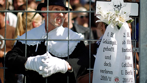 St. Paulis Fans halten ein Kreuz mit Trauerschleife hoch. © dpa 