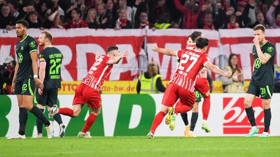 Wolfsburgs Felix Nmecha, Maximilian Arnold und Yannick Gerhardt (v.l.) sind enttäuscht, während Freiburgs Spieler jubeln. © IMAGO / Beautiful Sports 