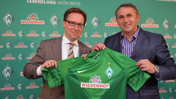 Werder-Geschäftsführer Klaus Allofs (rechts) hält mit dem Wiesenhof Geschäftsführer für Marketing Ingo Stryck das neue Werder Bremen-Tikot mit Wiesenhof-Aufdruck in den Händen. © dpa-Bildfunk Foto: Carmen Jaspersen