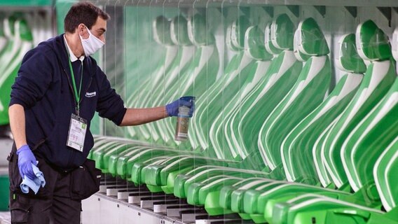 Ein Helfer reinigt und desinfiziert die Scheiben an der Auswechselbank des VfL Wolfsburg. © picture alliance/dpa | Swen Pförtner 