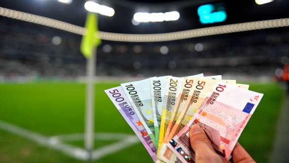 Eine Hand hält einige Geldscheine im Fußball-Stadion © imago images/MIS 