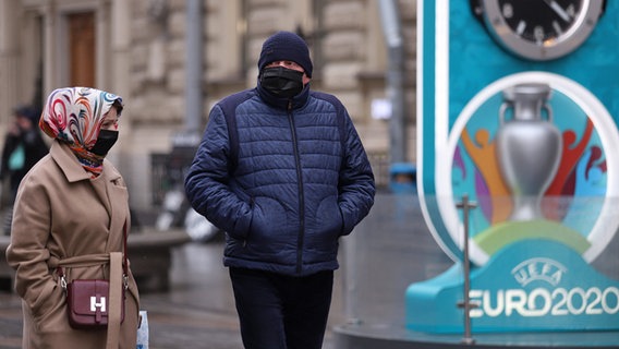 Passanten in St. Petersburg mit Mundschutz vor einem Emblem der EURO 2020 © imago images Foto: Sergei Mikhailichenko