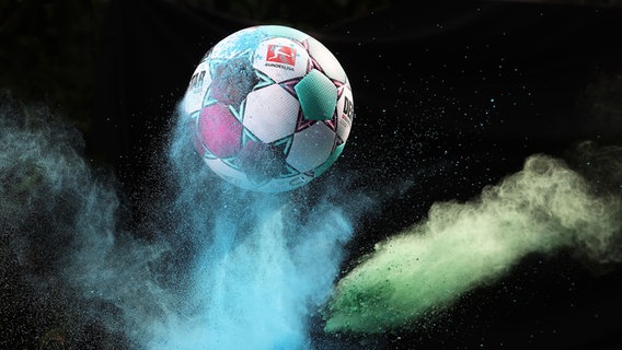 Ein Ball schießt in die Höhe, darunter blaues und grünes Farbpulver. Auf dem Ball: das Bundesliga-Logo. © picture alliance/augenklick Foto: firo Sportphoto/Jürgen Fromme