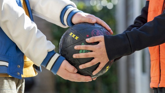 Kinder halten gemeinsam einen Fußball in den Händen. © IMAGO / ANP 