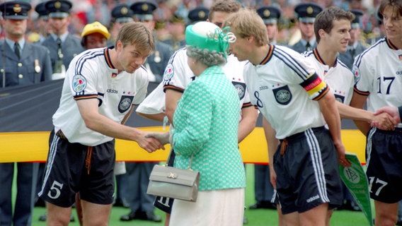 Thomas Helmer im Trikot der deutschen Fußballnationalmannschaft  wird von Queen Elizabeth II begrüßt, Kapitän Klinsmann stellt einander vor. © imago sportfotodienst 