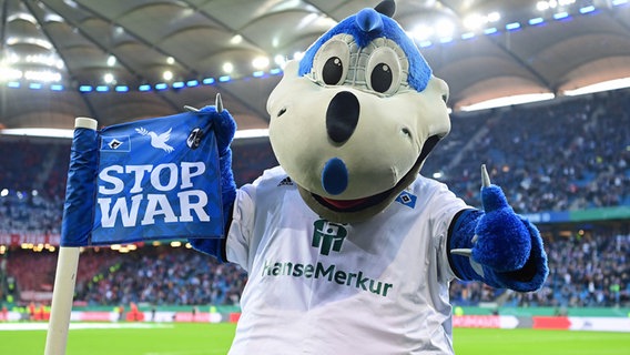 HSV-Maskottchen Dino Hermann und eine Eckfahne im Volksparkstadion mit der Aufschrift ''STOP WAR' © Witters 