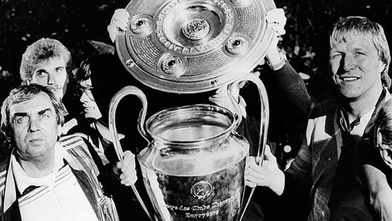 HSV-Trainer Ernst Happel (l.) und seine Spieler Thomas von Heesen (l.o.) und Horst Hrubesch (r.) mit der Meisterschale und dem Europacup der Landesmeister. © dpa - Sportreport 