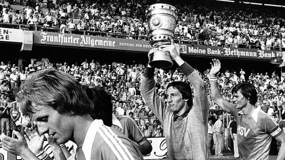 HSV-Torhüter Rudi Kargus (M.) läuft im Juni 1976 im Frankfurter Waldstadion vor 61.000 Zuschauern eine Ehrenrunde mit dem DFB-Pokal. Die Hamburger gewinnen die Trophäe durch einen 2:0-Erfolg über Kaiserslautern. © dpa 