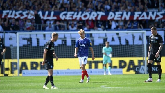 Holstein Kiels Tom Alexander Rothe im Spiel gegen Paderborn. Im Hintergrund haben Kiels Fans ein Transparent "Fussball gehört den Fans" entrollt. © picture alliance/dpa | Michael Schwartz 