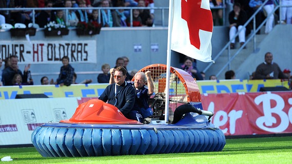 HSV-Physiotherapeut Hermann Rieger (h.) wird beim Tag der Legenden im Luftkissenboot auf den Platz gefahren. © dpa 