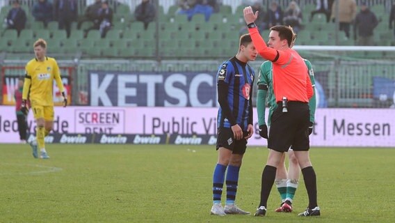 Schiedsrichter Nico Fuchs unterbricht das Drittliga-Spiel zwischen dem VfB Lübeck und Waldhof Mannheim nach Schneeballwürfen aufs Feld © IMAGO / Nordphoto 