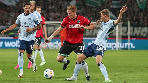 Hannovers Marcel Halstenberg (M.) behauptet den Ball gegen den Hamburger Ignace van der Brempt (r.). © IMAGO / Jan Huebner 
