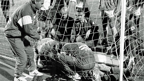 HSV-Abwehrspieler Ditmar Jakobs (verdeckt) liegt schwer verletzt im Torgehäuse - Helfer und HSV-Trainer Willi Reimann (l.) versuchen ihn zu befreien. © picture-alliance / dpa 