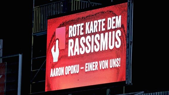Solidarität mit Aaron Opoku vom VfL Osnabrück auf der  Anzeigetafel bei den Würzburger Kickers. © IMAGO / Beautiful Sports 