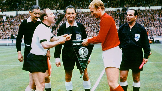 Uwe Seeler beim Wimpeltausch mit Englands Kapitän Bobby Moore vor dem WM-Finale 1966. In der Mitte: Schiedsrichter Gottfried Dienst. © dpa 