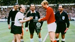 Uwe Seeler beim Wimpeltausch mit Englands Kapitän Bobby Moore vor dem WM-Finale 1966. In der Mitte: Schiedsrichter Gottfried Dienst. © dpa 